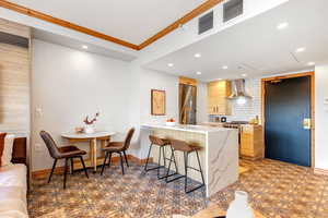 Kitchen with a peninsula, a kitchen breakfast bar, modern cabinets, light stone countertops, and crown molding