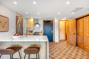 Kitchen featuring a breakfast bar, light stone counters, light brown cabinets, decorative backsplash, and a peninsula