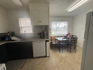 Kitchen featuring white dishwasher, freestanding refrigerator, white cabinetry, and light stone counters