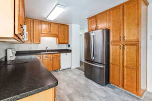 Kitchen featuring white appliances, dark countertops, and brown cabinetry