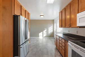 Kitchen featuring white appliances, dark countertops, and brown cabinetry