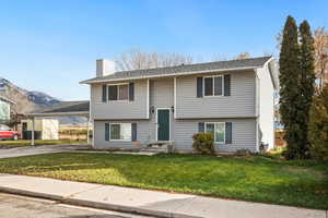 Raised ranch featuring a front lawn, a chimney, a shingled roof, and driveway