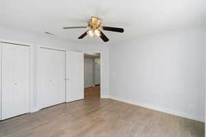 Unfurnished bedroom with multiple closets, light wood finished floors, a ceiling fan, and freestanding refrigerator