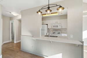 Kitchen with white cabinets, white appliances, tasteful backsplash, a breakfast bar area, and light wood-style floors