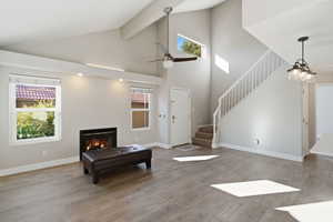 Living area featuring stairs, a glass covered fireplace, high vaulted ceiling, light wood-style floors, and a ceiling fan