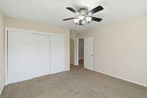 Unfurnished bedroom with carpet flooring, a closet, ceiling fan, and arched walkways
