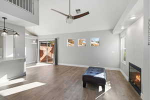 Living area featuring ceiling fan, a glass covered fireplace, wood finished floors, lofted ceiling, and recessed lighting