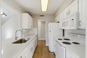 Kitchen with white appliances, white cabinetry, backsplash, light wood-style floors, and light stone countertops