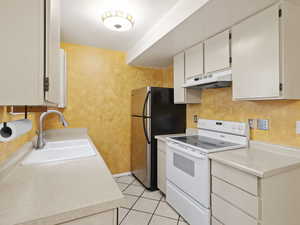 Kitchen featuring electric range, light countertops, under cabinet range hood, light tile patterned floors, and white cabinets