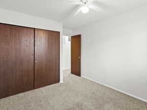 Unfurnished bedroom with a textured ceiling, carpet, a closet, and ceiling fan