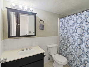 Bathroom with vanity, curtained shower, tile walls, a wainscoted wall, and light tile patterned floors