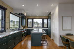 Kitchen with green cabinetry, a center island, high end appliances, a breakfast bar area, and light wood-type flooring