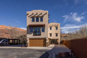 Pueblo revival-style home with concrete driveway, stucco siding, an attached garage, a mountain view, and stone siding