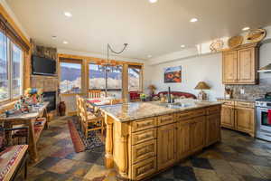 Kitchen with light stone counters, a fireplace, recessed lighting, tasteful backsplash, and a kitchen island with sink