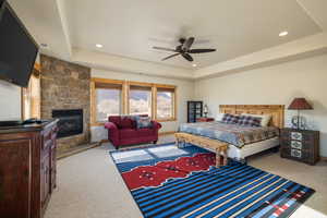 Bedroom with light carpet, a fireplace, a raised ceiling, a ceiling fan, and recessed lighting