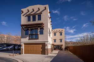 Pueblo-style house featuring concrete driveway, stone siding, stucco siding, an attached garage, and a mountain view