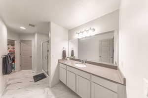 Bathroom featuring a walk in closet, vanity, a shower stall, light marble finish flooring, and recessed lighting