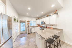 Kitchen with stainless steel appliances, white cabinets, a kitchen bar, a peninsula, and light wood-style flooring