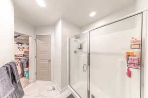 Bathroom with a stall shower, a spacious closet, light marble finish floors, and recessed lighting
