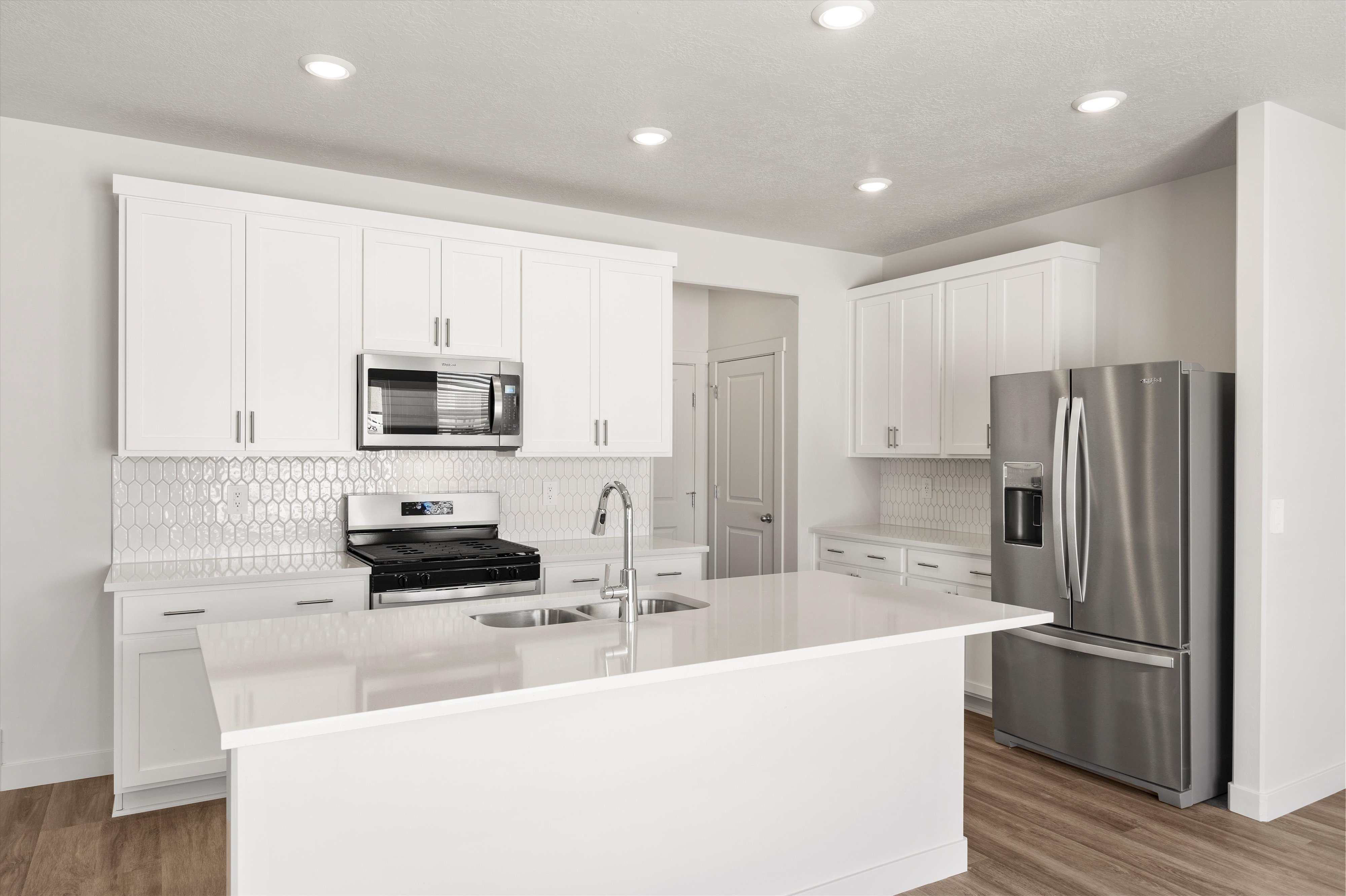 **DISLCAIMER** Exterior & Interior packages may vary.Kitchen featuring backsplash, appliances with stainless steel finishes, white cabinetry, a kitchen island with sink, and recessed lighting