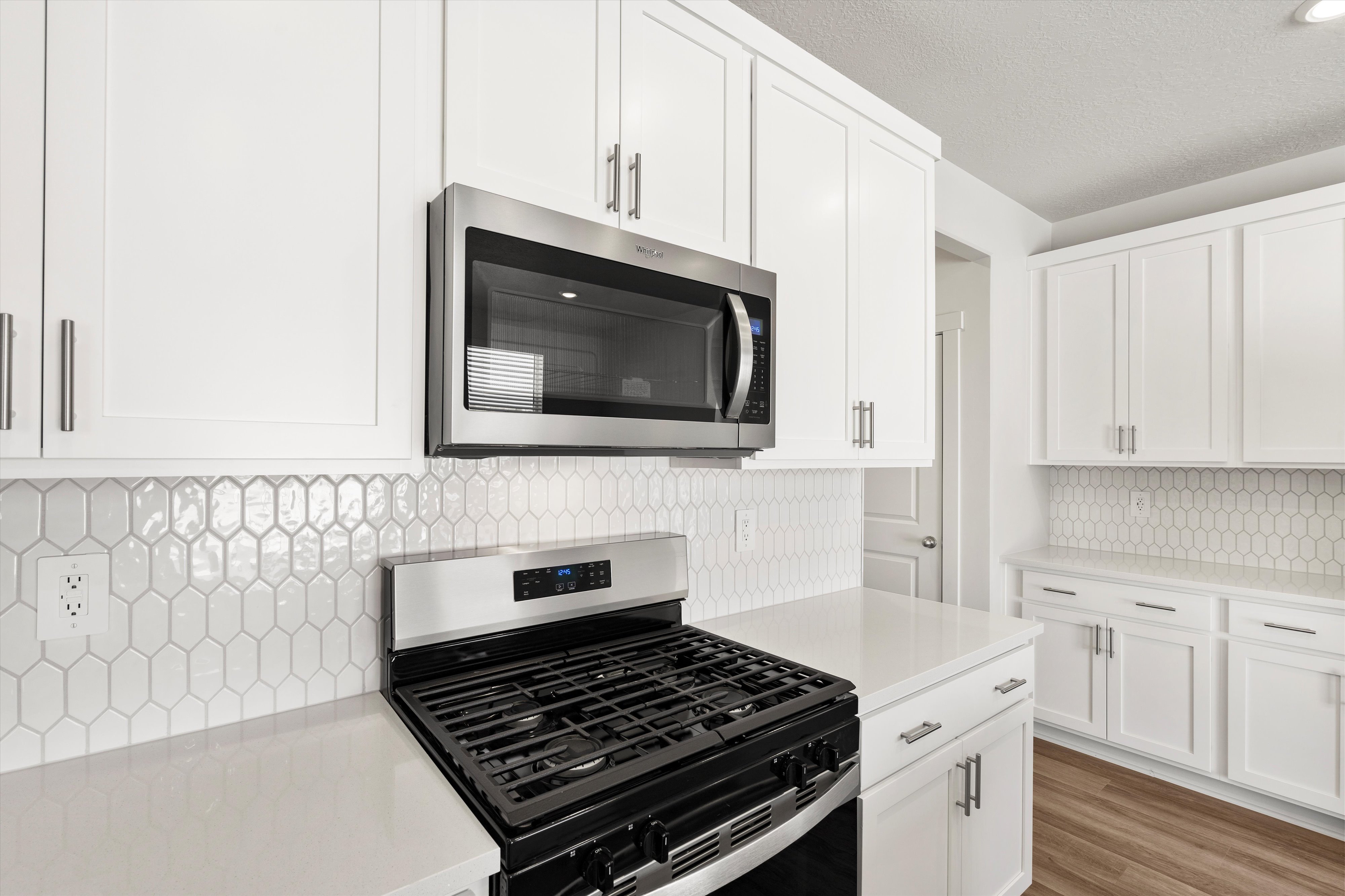 **DISLCAIMER** Exterior & Interior packages may vary.Kitchen with stainless steel appliances, white cabinetry, backsplash, a textured ceiling, and light stone counters