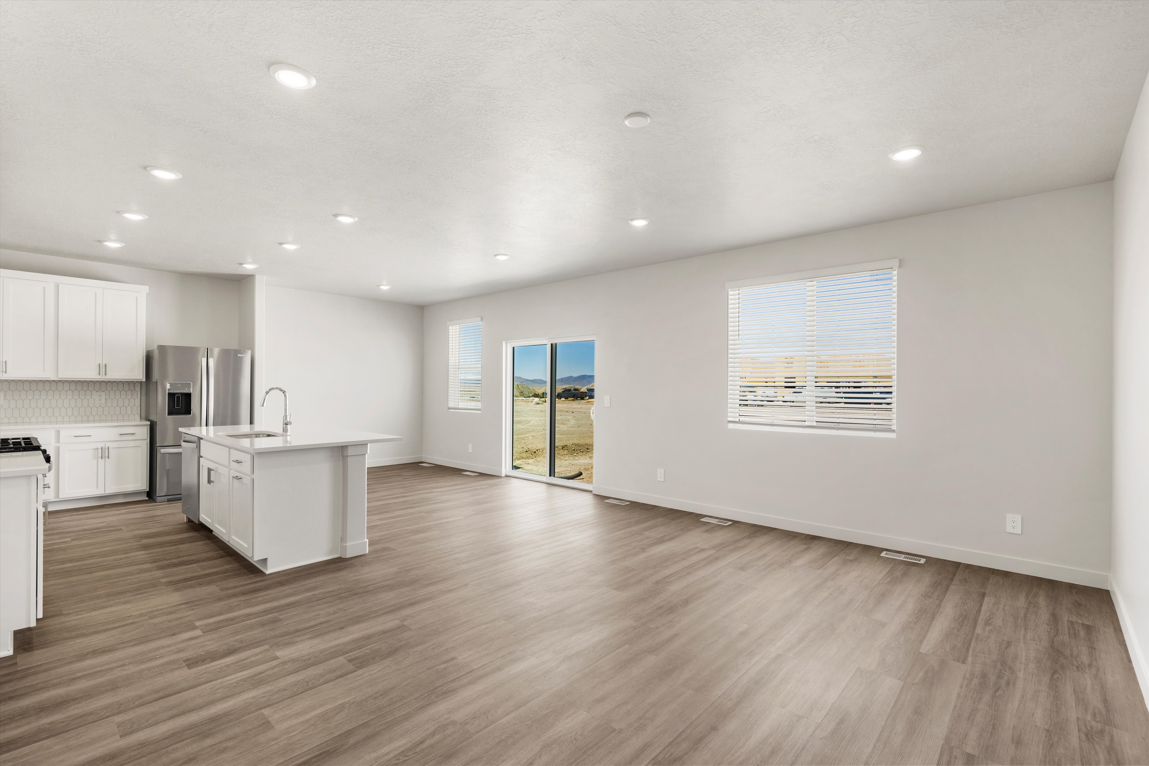 **DISLCAIMER** Exterior & Interior packages may vary.Kitchen featuring white cabinets, decorative backsplash, open floor plan, a kitchen island with sink, and light wood-type flooring