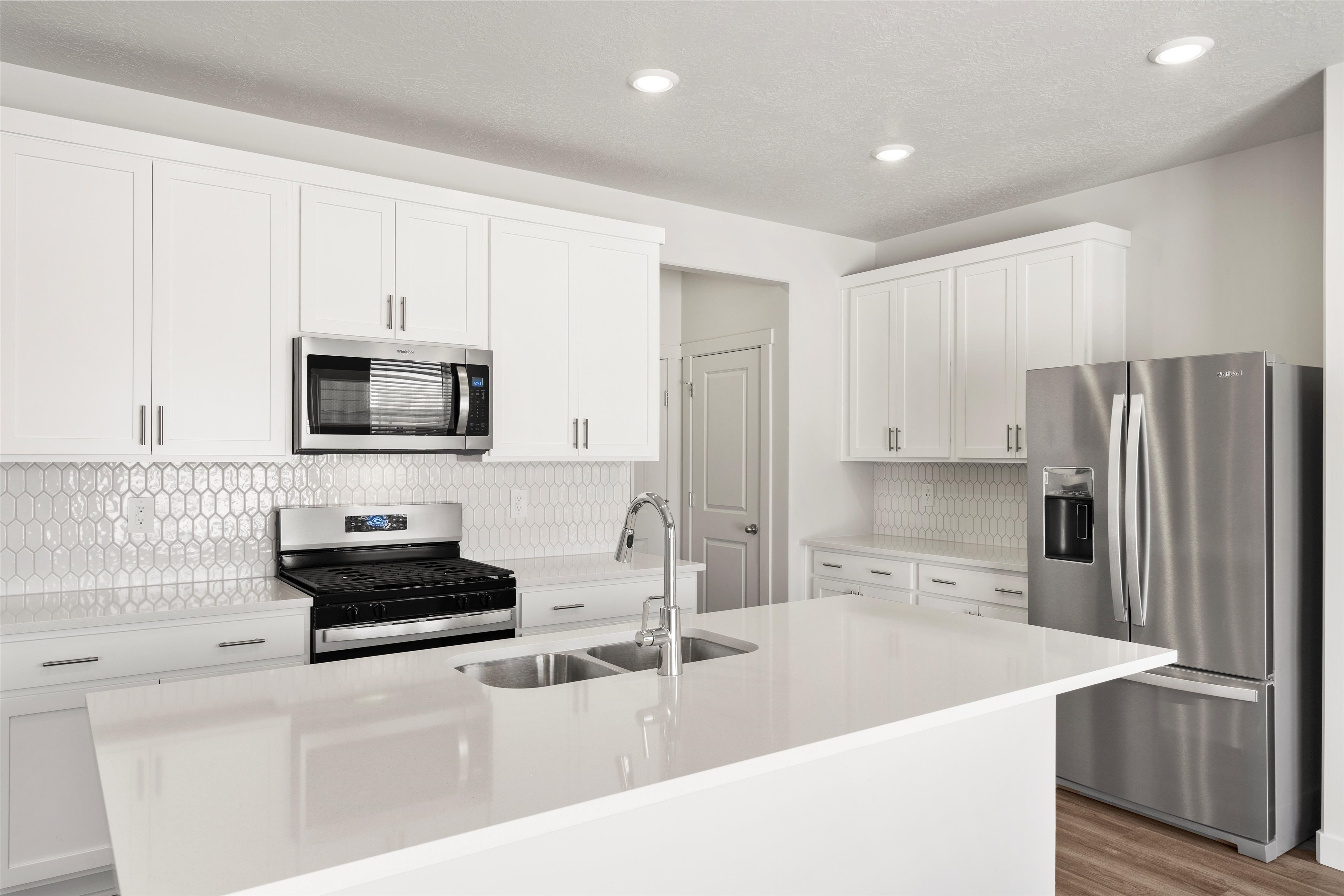 **DISLCAIMER** Exterior & Interior packages may vary.Kitchen with backsplash, appliances with stainless steel finishes, white cabinets, a kitchen island with sink, and recessed lighting