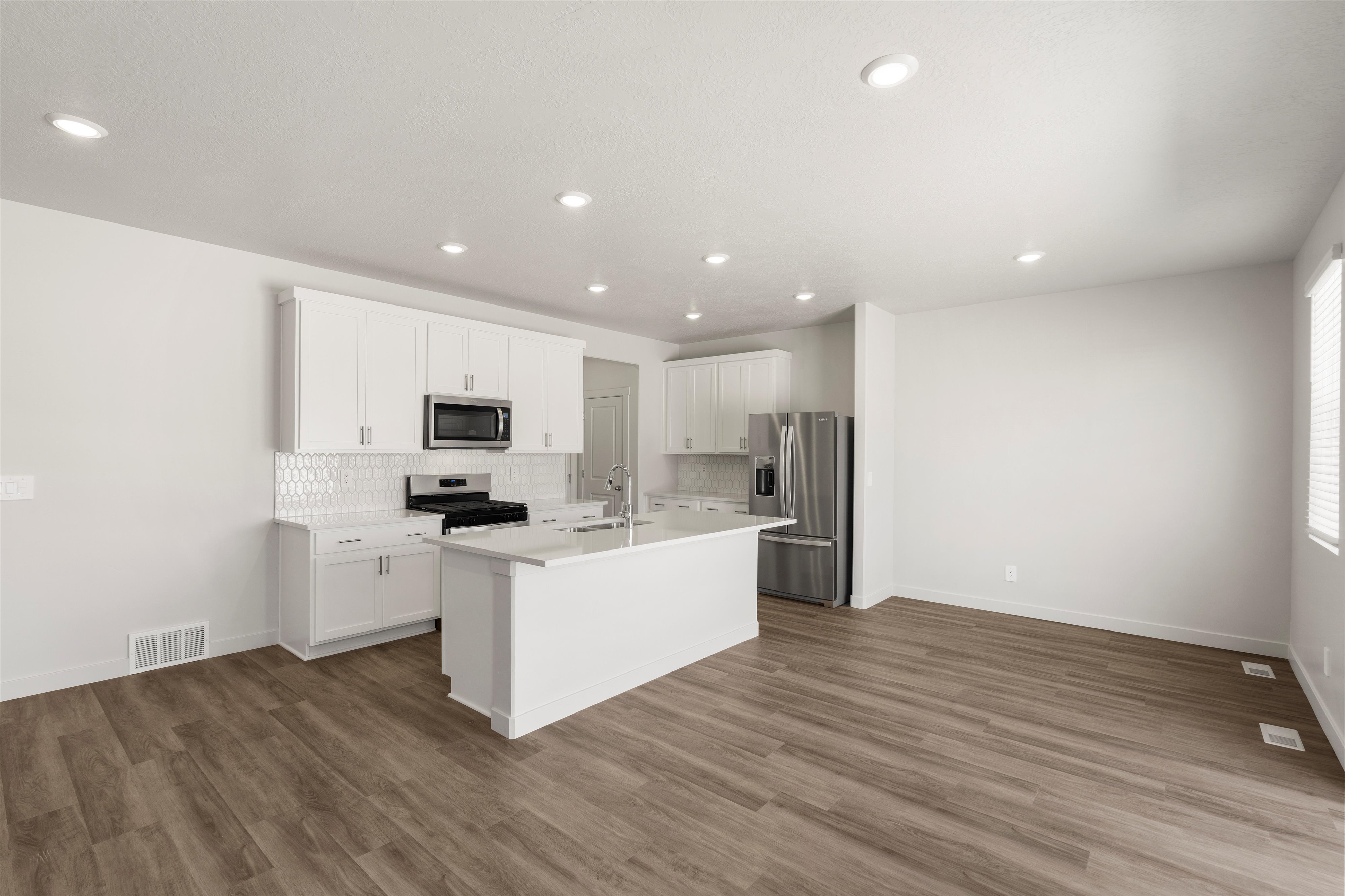 **DISLCAIMER** Exterior & Interior packages may vary.Kitchen featuring white cabinetry, appliances with stainless steel finishes, an island with sink, decorative backsplash, and dark wood-type flooring