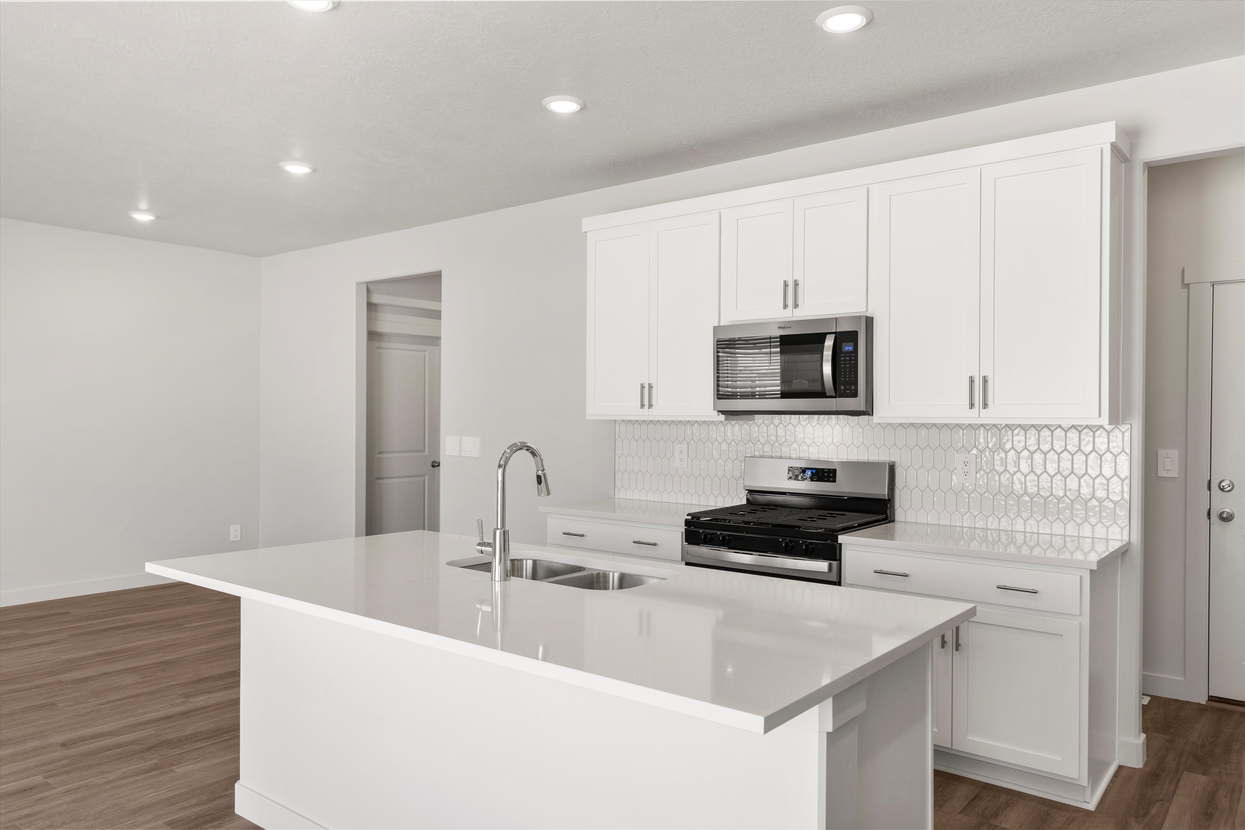 **DISLCAIMER** Exterior & Interior packages may vary.Kitchen with appliances with stainless steel finishes, a center island with sink, white cabinets, dark wood-type flooring, and tasteful backsplash
