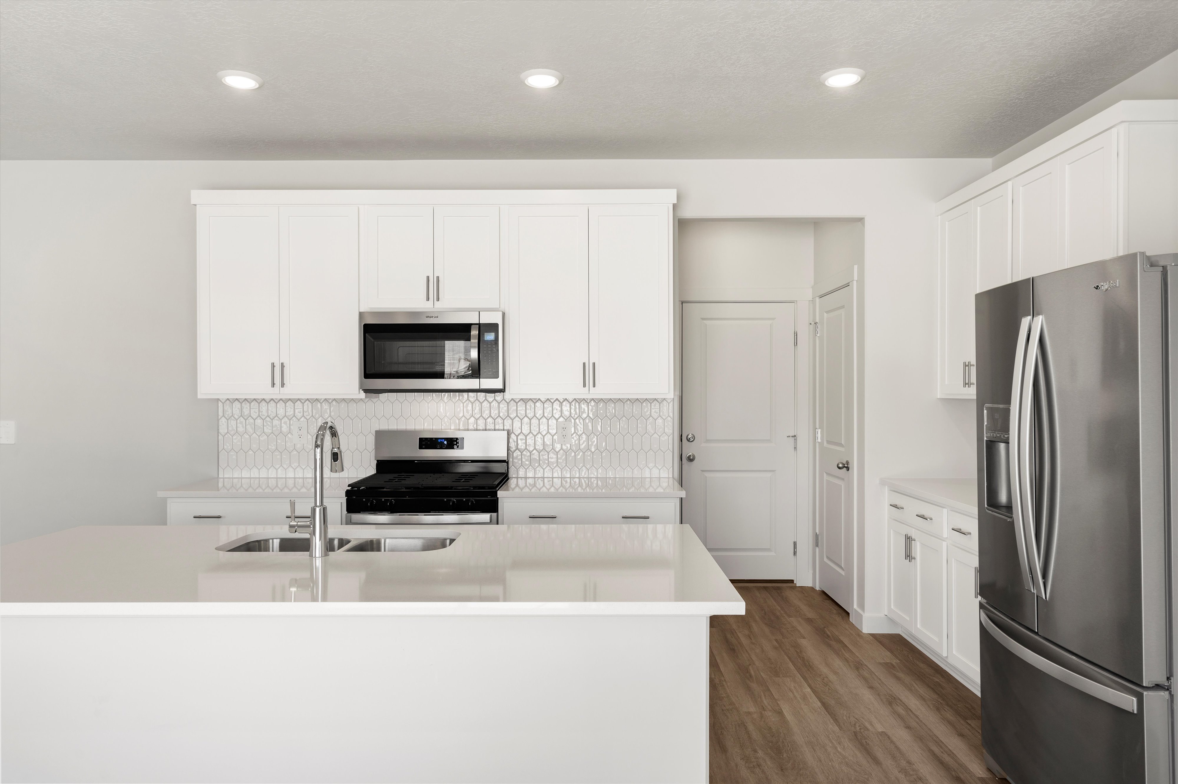**DISLCAIMER** Exterior & Interior packages may vary.Kitchen featuring appliances with stainless steel finishes, white cabinetry, an island with sink, decorative backsplash, and dark wood-style floors