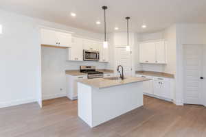 Kitchen featuring stainless steel appliances, white cabinets, and light wood-style floors