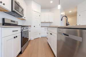 Kitchen with stainless steel appliances, light wood-type flooring, white cabinets, decorative light fixtures, and light countertops