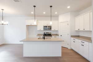 Kitchen featuring white cabinetry, a center island with sink, stainless steel appliances, and light wood-type flooring