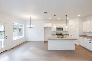 Kitchen featuring white cabinetry, stainless steel appliances, a center island with sink, and light wood-style floors