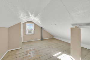 Bonus room with vaulted ceiling, a textured ceiling, and light wood finished floors