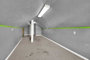 Additional living space featuring carpet flooring, a textured ceiling, and vaulted ceiling