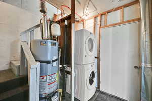 Washroom with strapped water heater, stacked washing machine and dryer, and concrete flooring