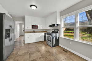 Kitchen with stainless steel appliances, white cabinetry, healthy amount of natural light, and under cabinet range hood