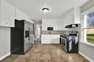 Kitchen with appliances with stainless steel finishes, light countertops, under cabinet range hood, and white cabinets