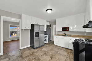 Kitchen featuring black gas stove, stainless steel fridge, white cabinets, under cabinet range hood, and light countertops