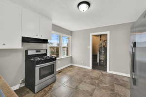 Kitchen featuring stainless steel appliances, white cabinetry, secured water heater, and under cabinet range hood