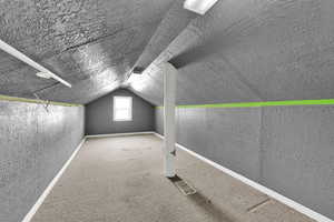 Additional living space with carpet floors, a textured wall, vaulted ceiling, and a textured ceiling