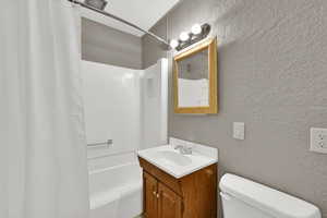 Bathroom with a textured wall, shower / bath combo with shower curtain, and vanity
