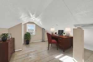 Office with light wood-type flooring, lofted ceiling, and a textured ceiling