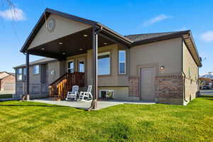 Back of property featuring brick siding, a patio area, stucco siding, and a lawn
