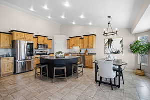 Kitchen featuring a kitchen breakfast bar, stainless steel appliances, a center island, hanging light fixtures, and dark stone countertops
