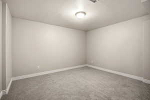 Carpeted empty room with a textured ceiling and baseboards