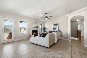 Living area with arched walkways, lofted ceiling, ceiling fan, and a lit fireplace