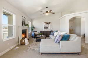 Living room featuring lofted ceiling, a glass covered fireplace, a ceiling fan, arched walkways, and carpet floors