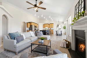 Living area featuring a fireplace with flush hearth, a ceiling fan, arched walkways, high vaulted ceiling, and light tile patterned floors